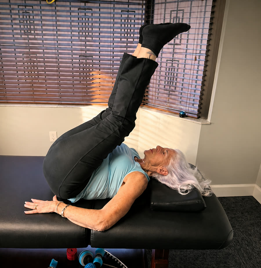 A 78-year-old StretchOut Wellness client holding an inverted leg raise on the treatment table